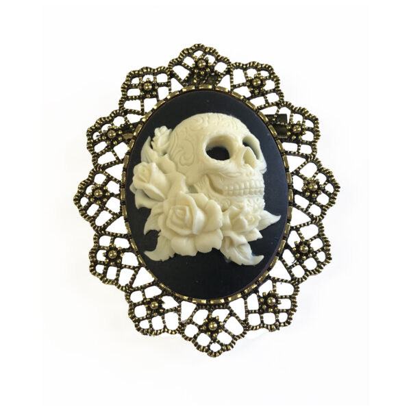 Jewelry Halloween Ivory color skull with roses on a black background in a gold lace brooch setting. Setting measures 2-1/4″x 2″.